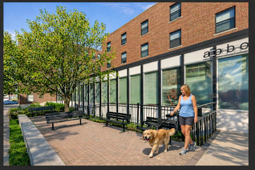 A woman walking her dog in front of a brick building.