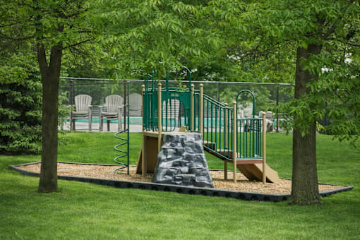 A playground with a green slide and a brown rock-like structure.