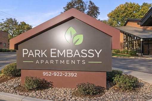A sign for Park Embassy Apartments with a phone number on it.