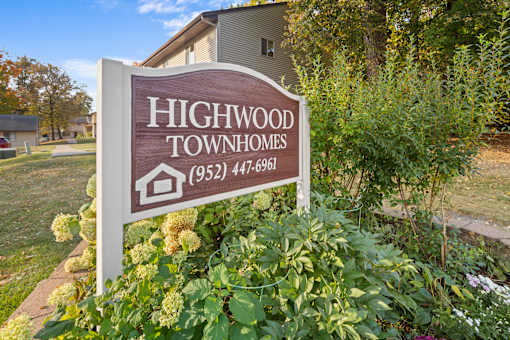 A sign for Highwood Townhomes stands in front of a building and some trees.