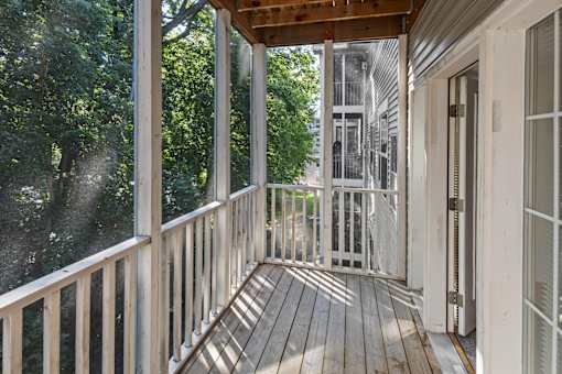 A wooden deck with a railing and a view of trees and a building in the background.