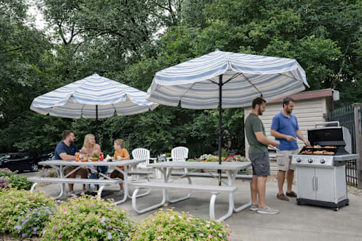 A group of people are gathered around a table under a striped umbrella.