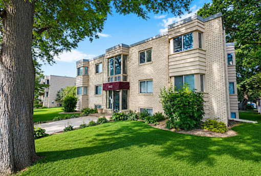 A large beige building with a red awning is surrounded by a green lawn.