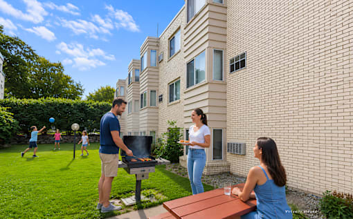 A man grilling in a backyard with a woman and children playing in the background.