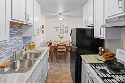 A kitchen with a black refrigerator, white cabinets, and a marble countertop.