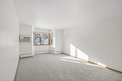 A large empty room with a window and a carpet on the floor.