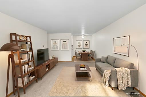 A living room with a grey couch, a coffee table, a bookshelf, and a lamp.