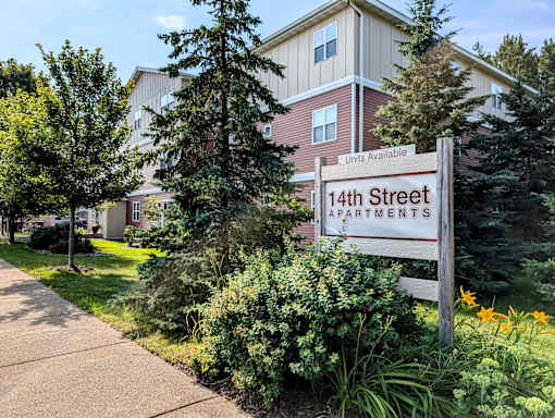 A sign for 14th Street Apartments is in front of a building with a well-kept lawn and trees.