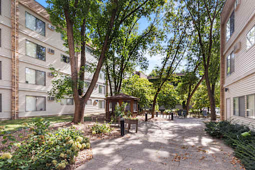 A tree-lined walkway leads to a small pavilion in a courtyard.