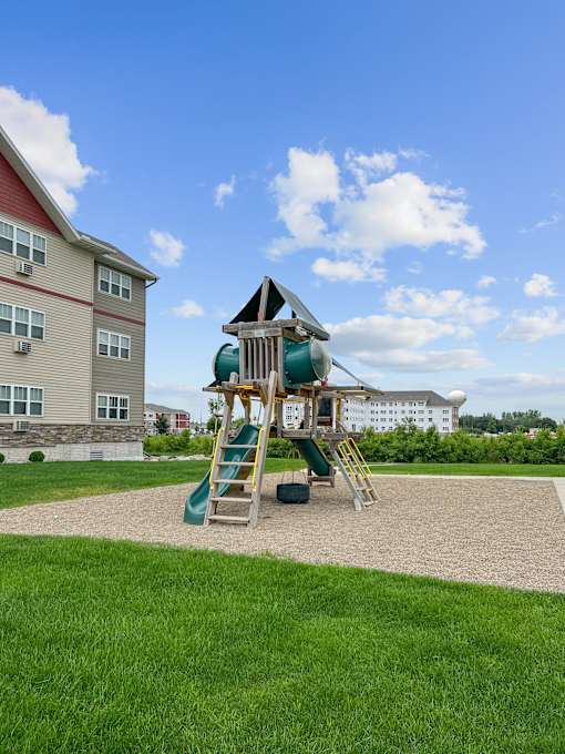 A playground with a green slide and a wooden ladder.