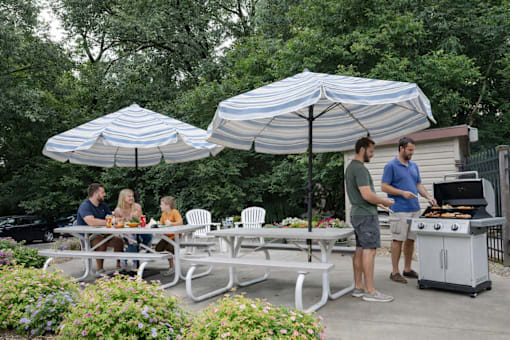 A group of people are gathered around a table under a striped umbrella.