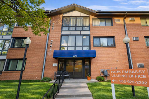 The image shows a brick building with a sign that reads "PARK EMBASSY LEASING OFFICE" and a phone number.