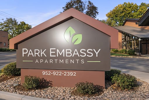 A sign for Park Embassy Apartments with a phone number on it.