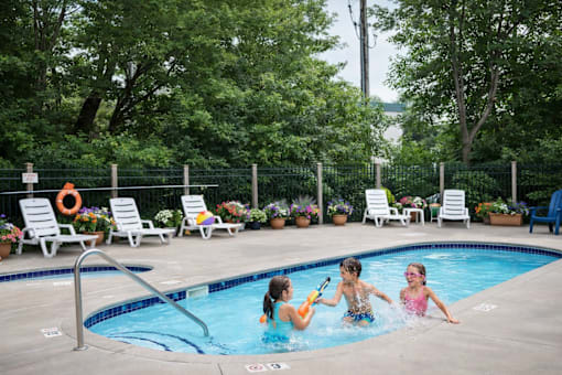Three children playing in a pool surrounded by lounge chairs and greenery.