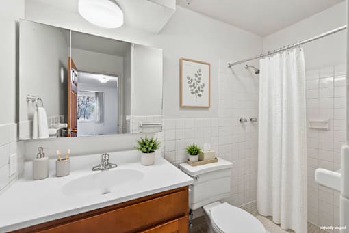 A white bathroom with a wooden vanity and a white toilet.