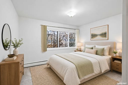 A bedroom with a large bed, a wooden dresser, and a window with a view of trees outside.