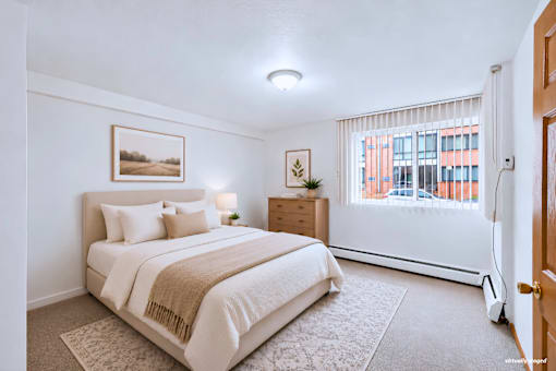 A bedroom with a large bed and a window with blinds.