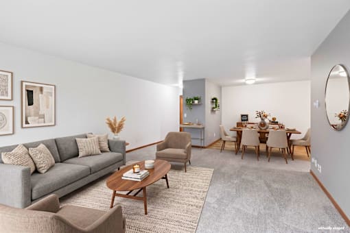 A living room with a grey couch, a wooden coffee table, and a dining table set up.