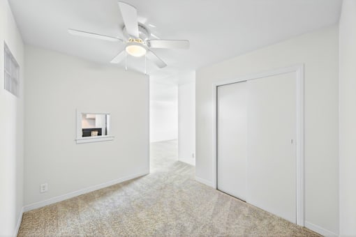 A room with a ceiling fan and a window with a picture frame on the wall.