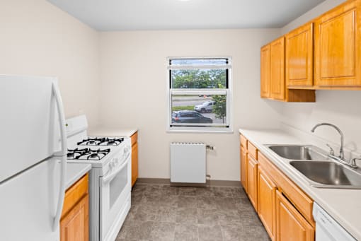 A kitchen with a white fridge, white stove, and a window with a view of the street.