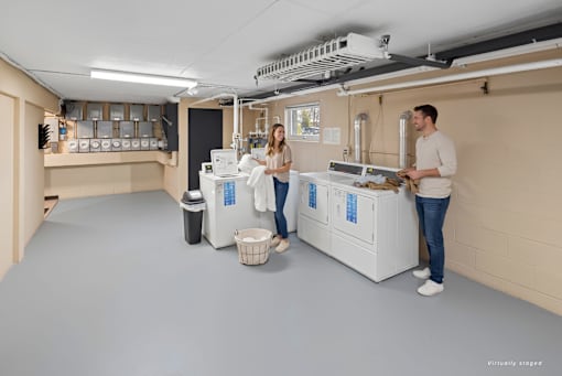 Two people in a room with a large machine and a basket on the floor.