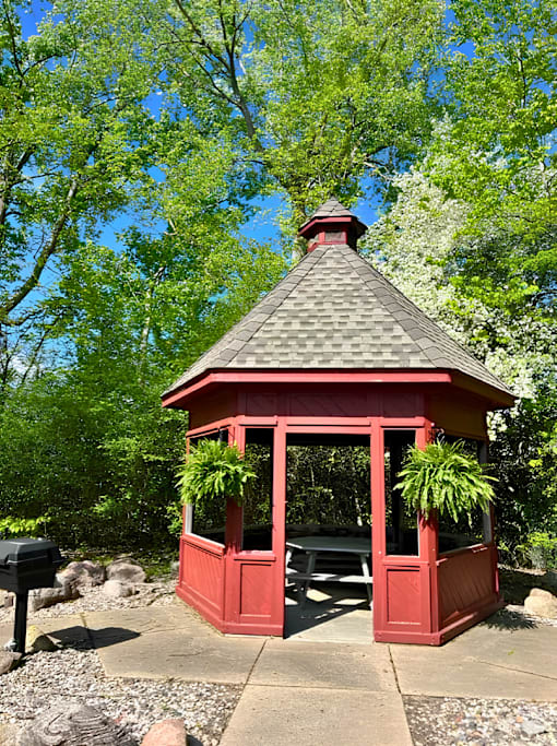 A red gazebo with a black roof is surrounded by trees.