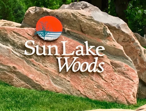 A large rock with the words Sun Lake Woods written on it.