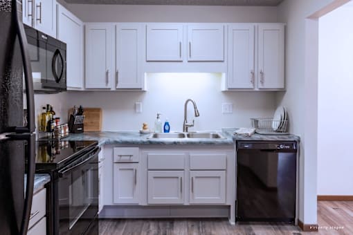 A kitchen with white cabinets and a black refrigerator.