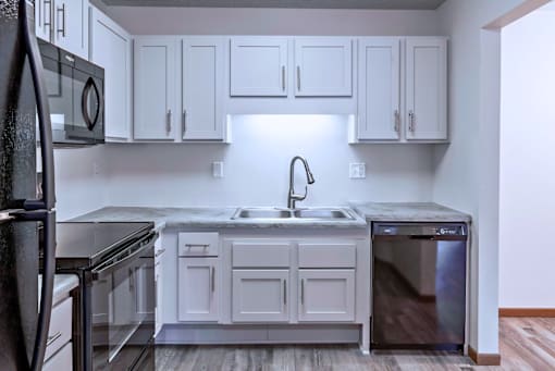 A kitchen with white cabinets and black appliances.