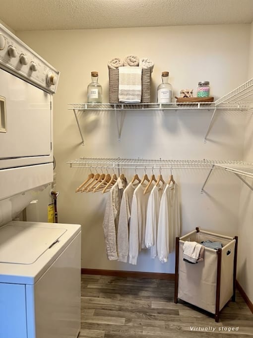 A laundry room with a washer and dryer, shelves with towels and other items, and clothes hanging on a rack.