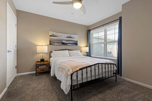 A bedroom with a large bed, a ceiling fan, and a painting on the wall.