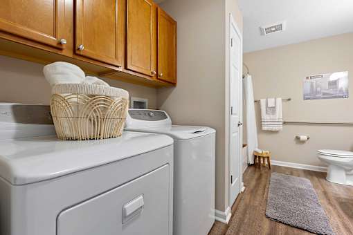 A laundry room with a washer and dryer, a basket of towels, and a rug on the floor.