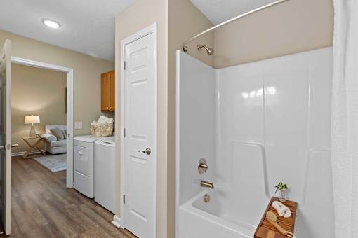 A bathroom with a white tub and a wooden tray with a plant on it.