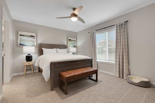 A bedroom with a bed, bench, and a ceiling fan.