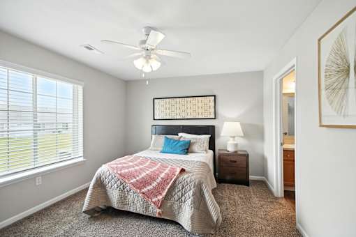 A bedroom with a bed, a ceiling fan, and a window with blinds.