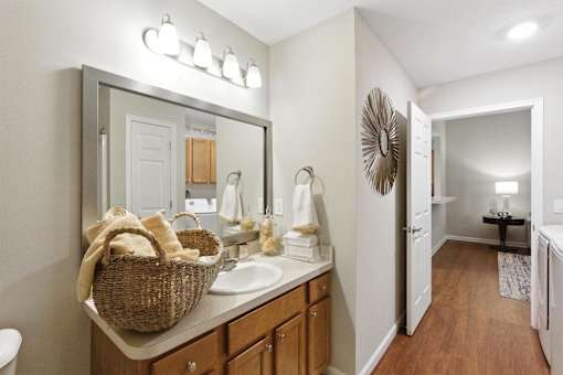 A bathroom with a mirror, sink, and a basket of towels.