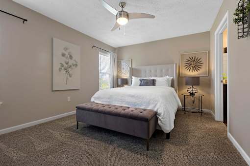 A bedroom with a bed, bench, and a ceiling fan.