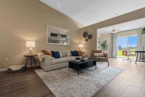A well-lit living room with a grey sofa, a coffee table, and a large window.