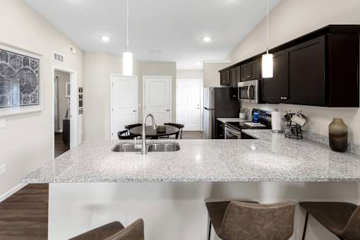 A kitchen with a granite countertop and brown chairs.