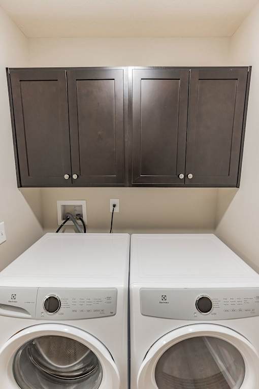 Two white washing machines in a laundry room with dark brown cabinets.
