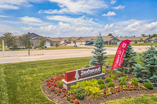 A Redfin sign is in front of a landscaped area with a flag.