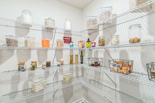 A white pantry with shelves full of food and drinks.