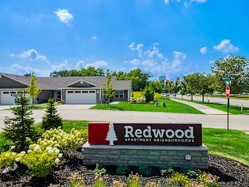 A sign for Redwood Apartment Neighborhoods is in the foreground of a well-kept lawn.
