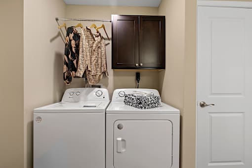 A laundry room with a white washer and dryer, a towel, and clothes hanging up.