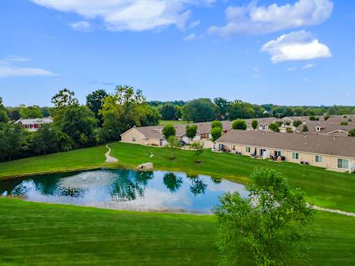A serene landscape with a pond, houses, and trees under a clear blue sky.
