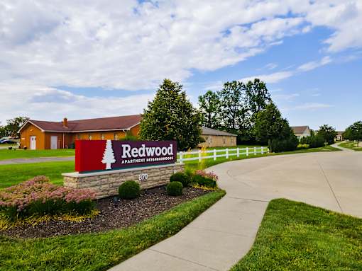 The image shows a sign for Redwood Apartment Homes in front of a building.