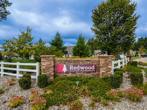 A sign for Redwood Estates is surrounded by a white fence and greenery.