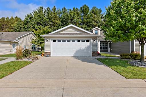 A house with a grey garage door is surrounded by greenery.