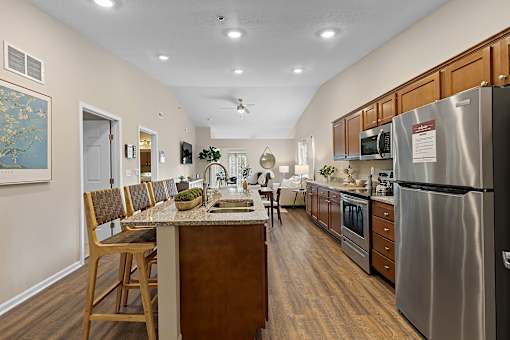 A kitchen with a refrigerator, sink, and wooden chairs.