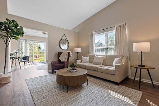 A living room with a white couch, a wooden coffee table, and a large window with white curtains.